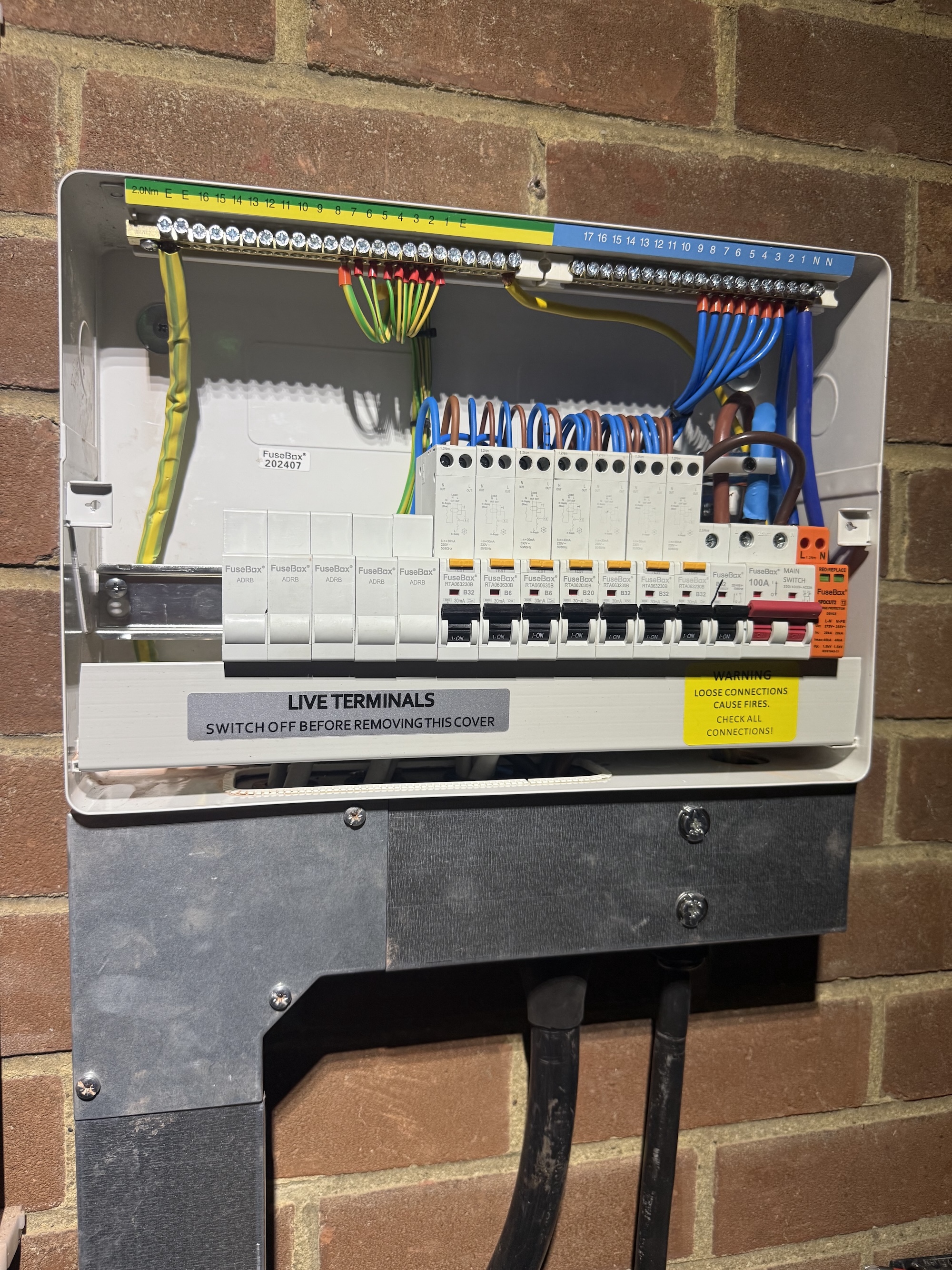 Open consumer unit with multiple circuit breakers and neatly organized colored wiring mounted on a brick wall.