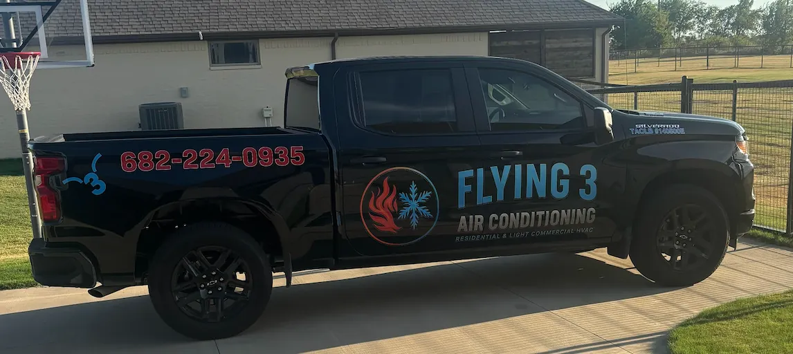 Black pickup truck with 'Flying 3 Air Conditioning' logo, contact number 682-224-0935, parked on driveway in front of house with fenced yard.