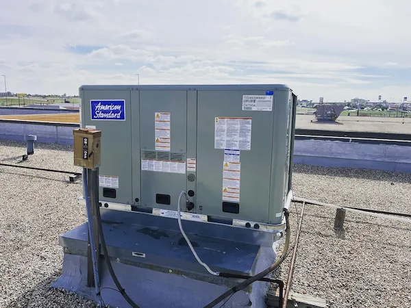 American Standard rooftop HVAC unit on a gravel-covered building roof under a cloudy sky.
