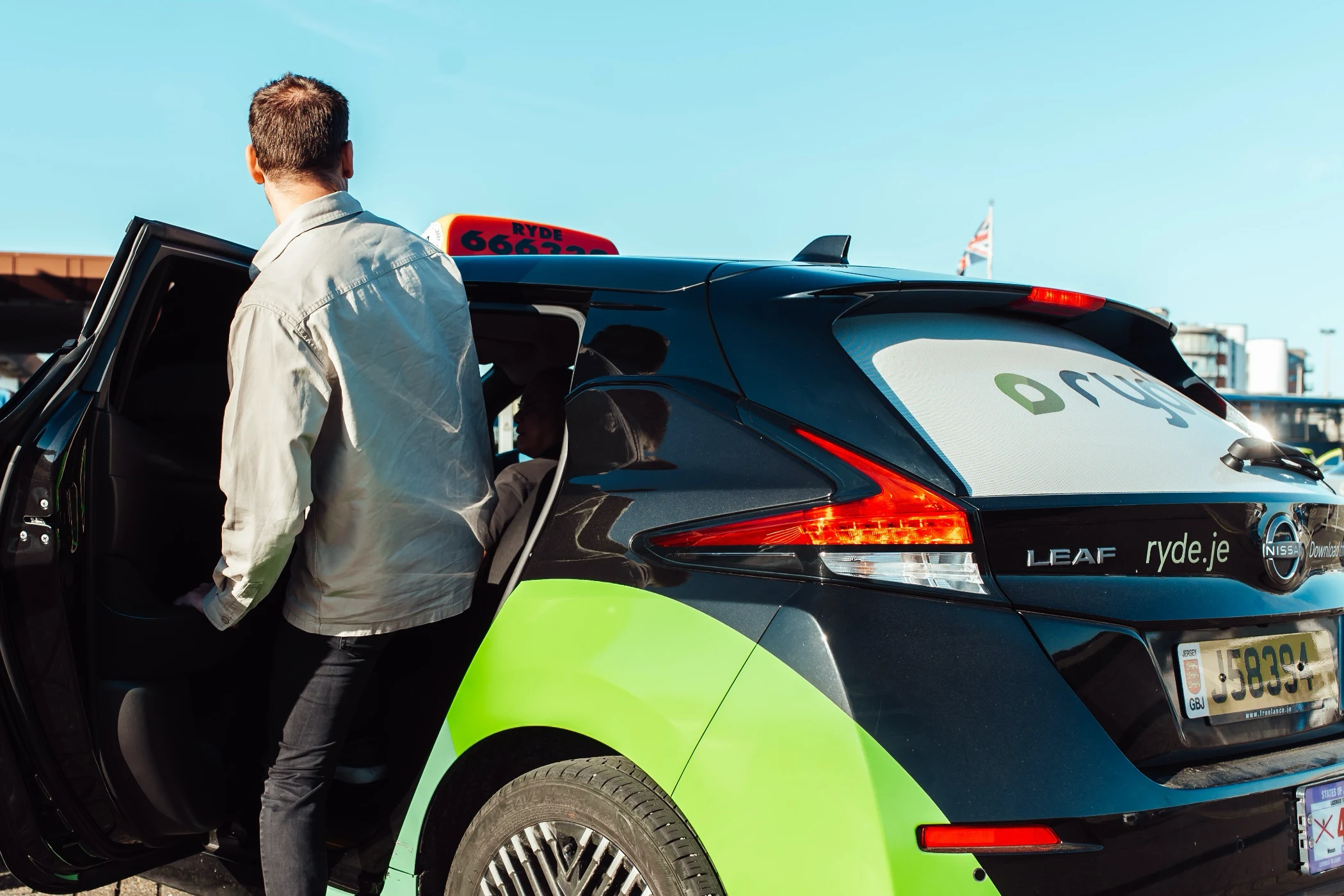 Person standing next to green and blue Nissan Leaf electric rideshare car