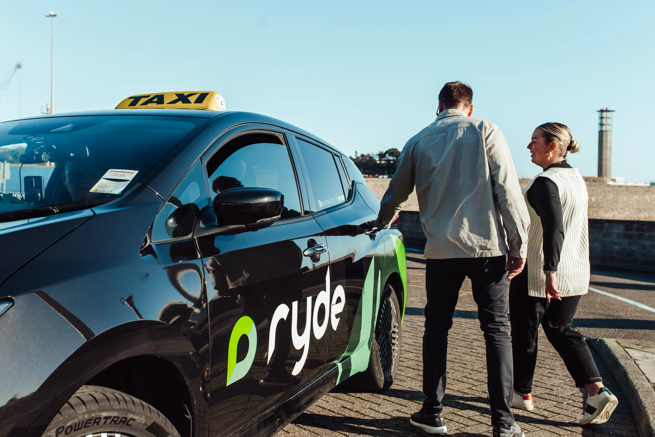 Two people standing next to a black and green Ryde taxi