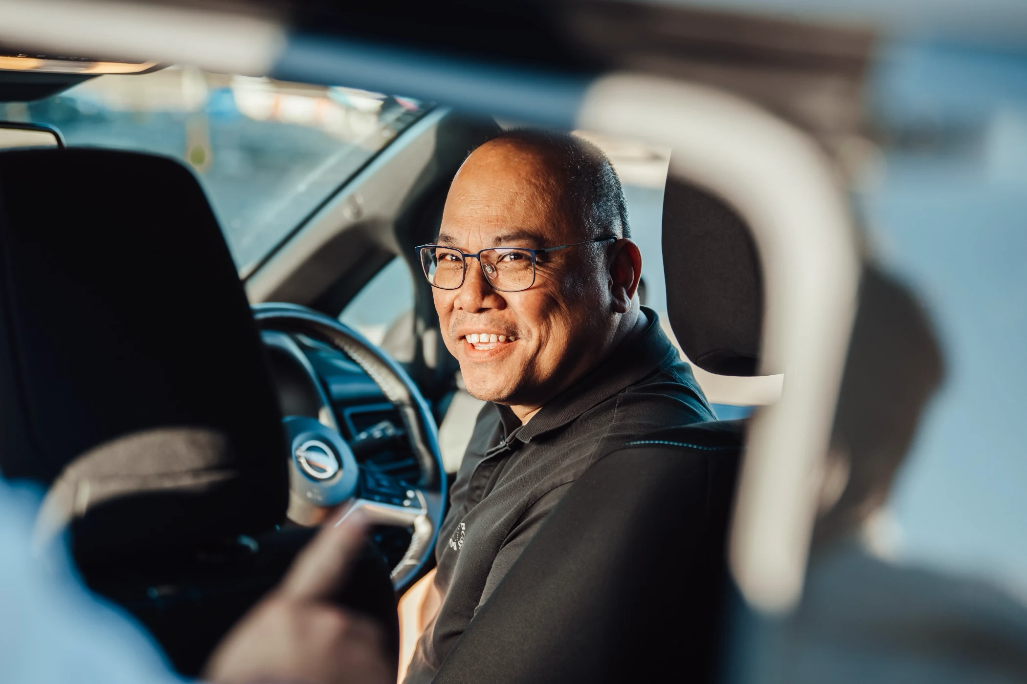 Smiling driver sitting in car, wearing glasses and black shirt