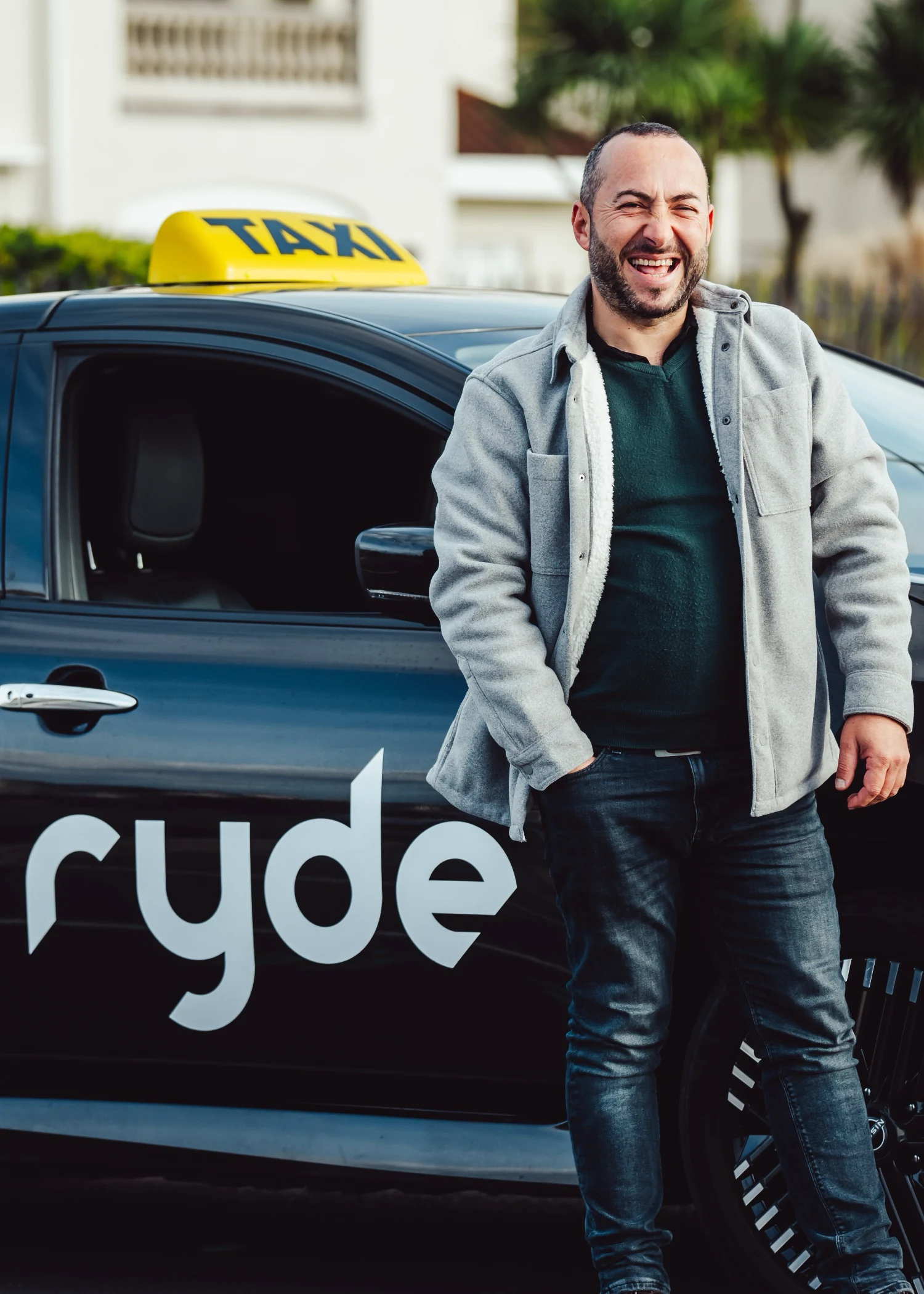 Smiling taxi driver standing next to Ryde vehicle with yellow taxi sign
