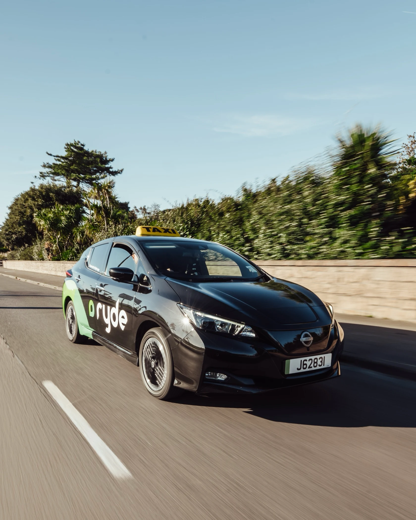 Black Ryde electric taxi driving on highway with blurred greenery background