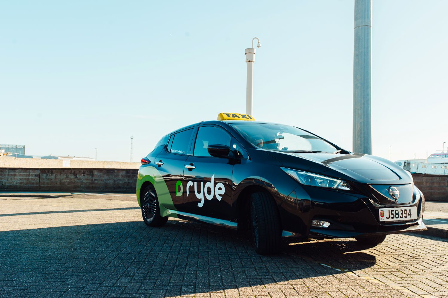 Black Nissan electric taxi with green and white Ryde branding parked on a sunny street.