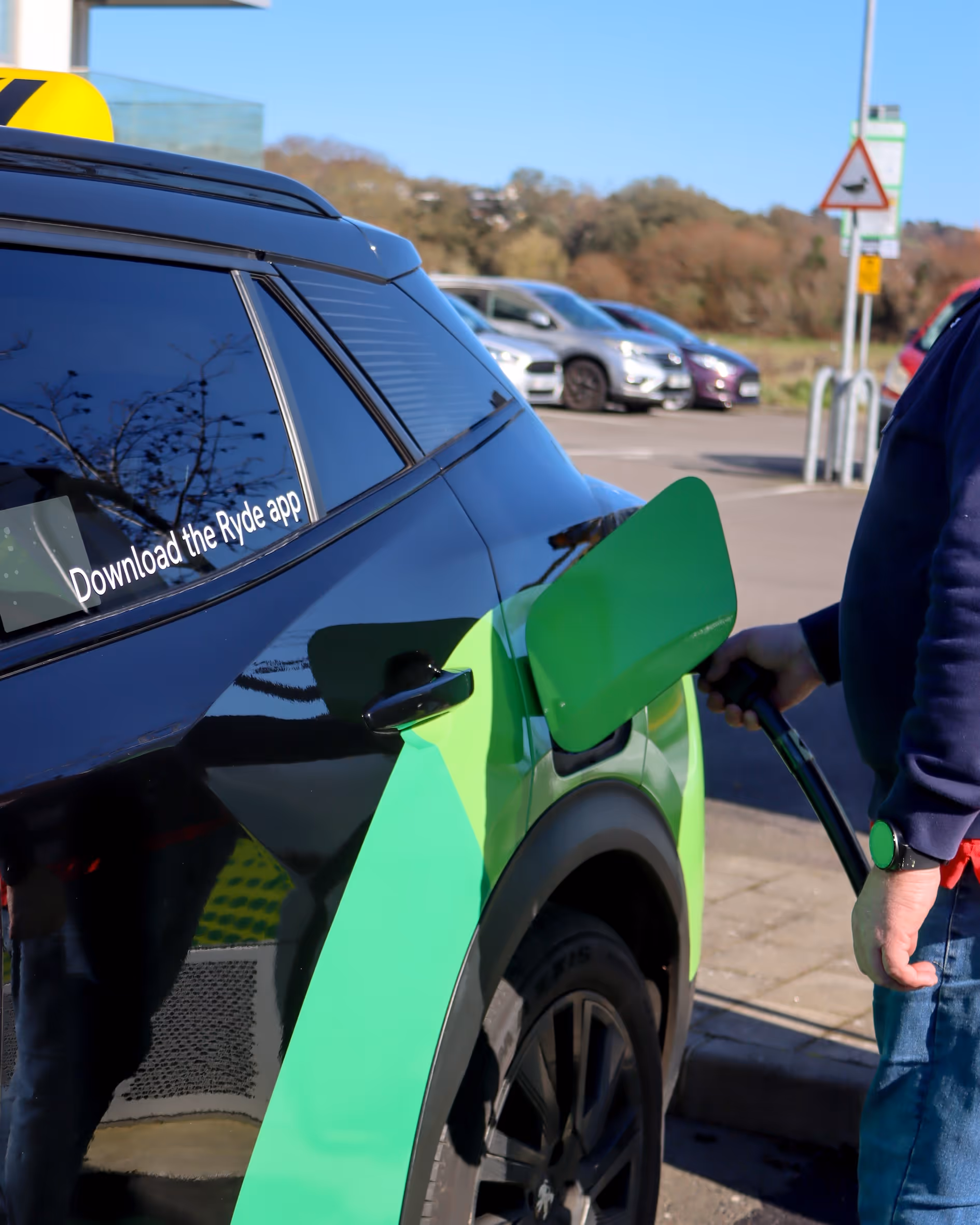 Person refueling a green and black electric car with 'Download the Ryde app' on its window.