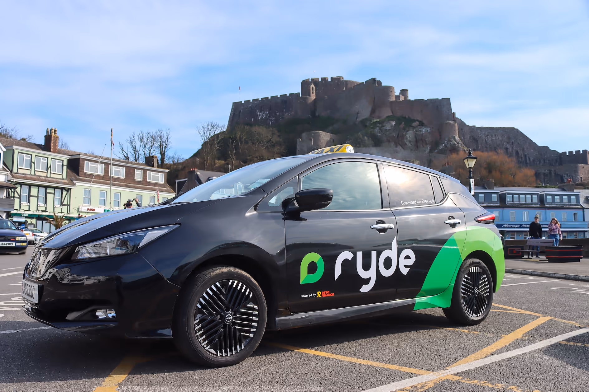 Black Ryde taxi car with green logo parked near a castle on a sunny day.
