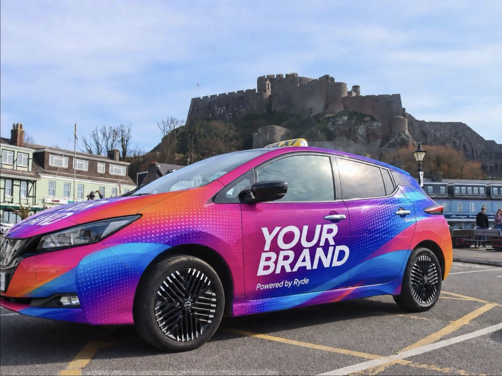Colorful car with 'YOUR BRAND Powered by Ryde' text parked near castle and buildings.