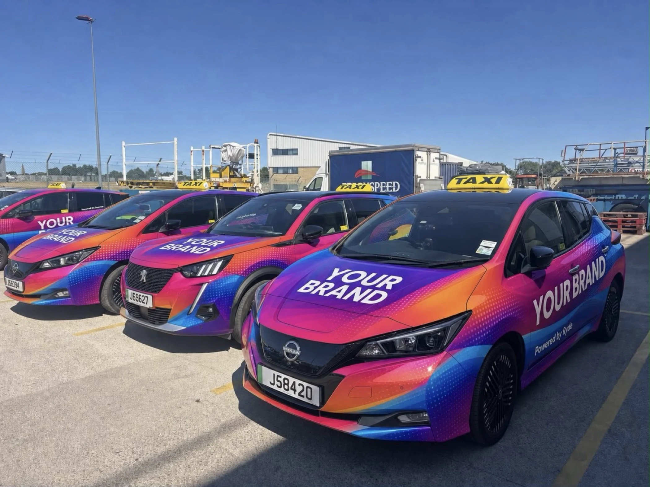 Three colorful taxis with 'YOUR BRAND' text and yellow taxi signs parked outdoors under clear sky.