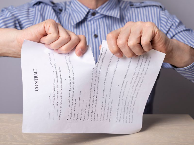 Person wearing a striped shirt tearing a contract document in half over a wooden table.