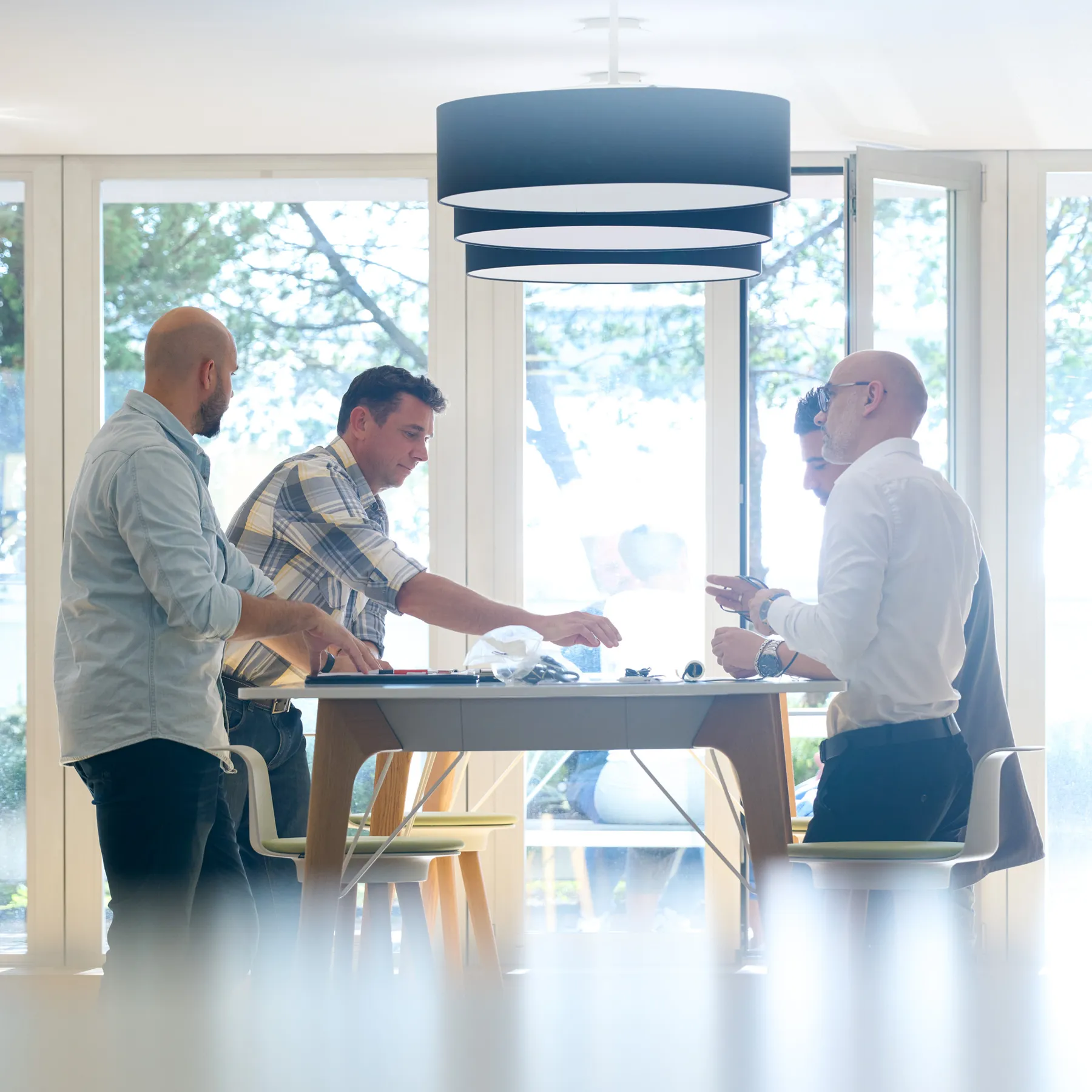 Four men in casual and business attire collaborating around a modern table in a bright room with large windows.