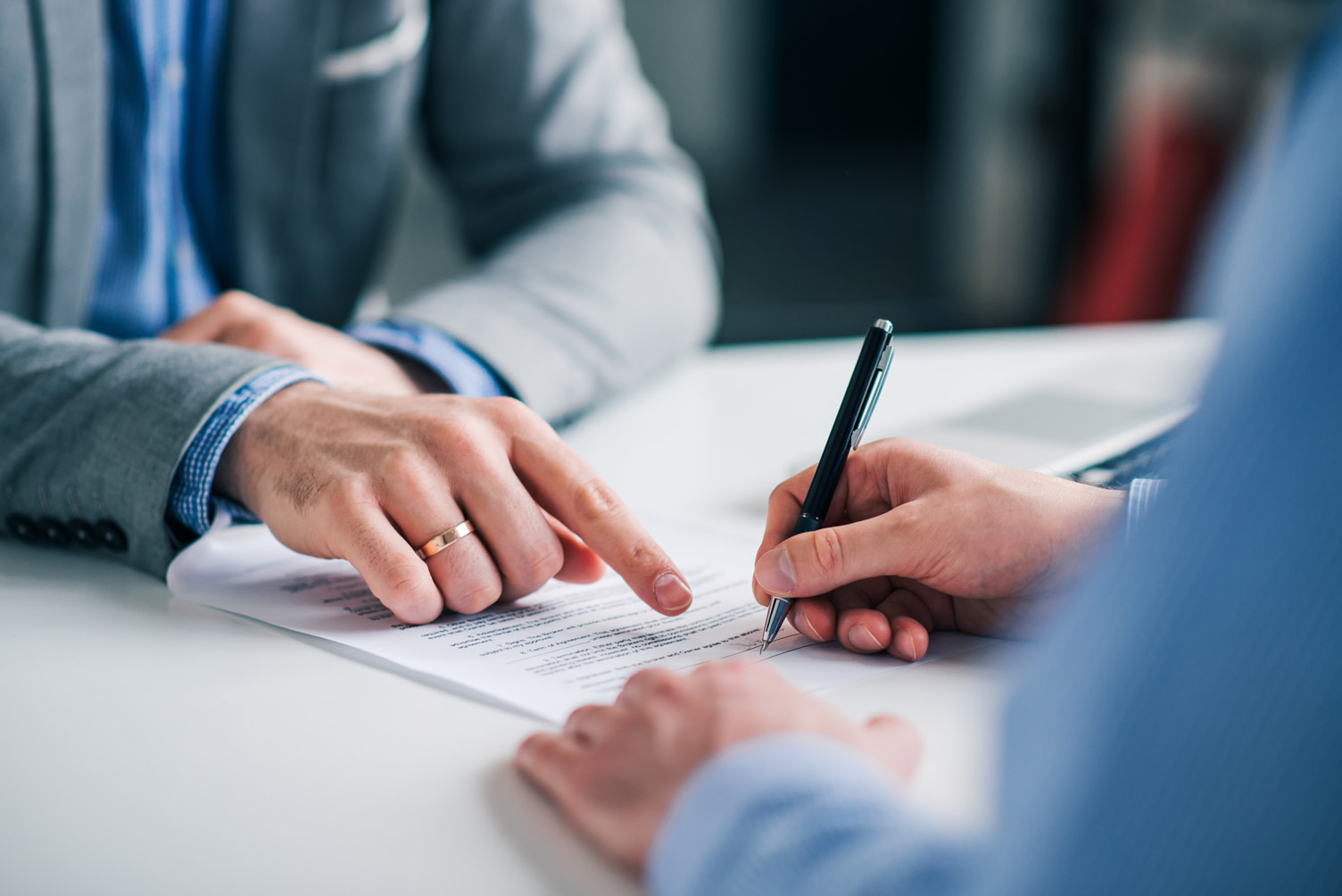 Two people at a table reviewing and signing a document, one person pointing at a section while the other holds a pen.