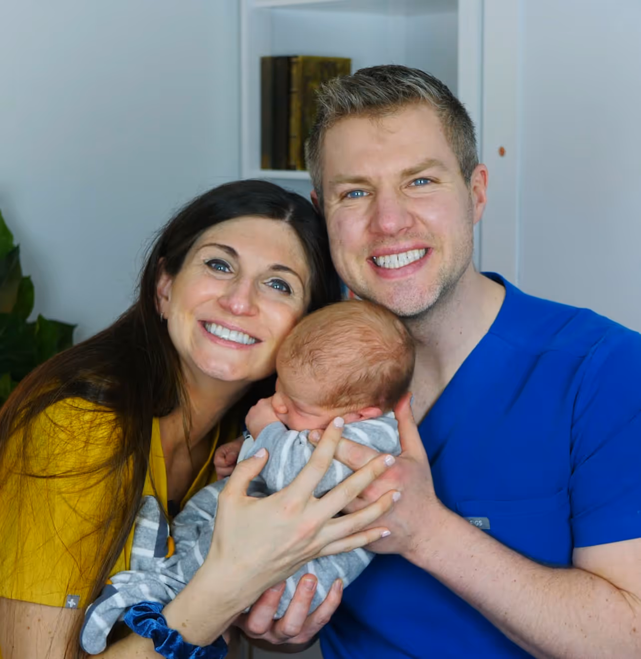 Dr. Sarah Bjorkman and Dr. Kurt Bjorkman smiling while holding their newborn baby wrapped in a gray and white striped blanket