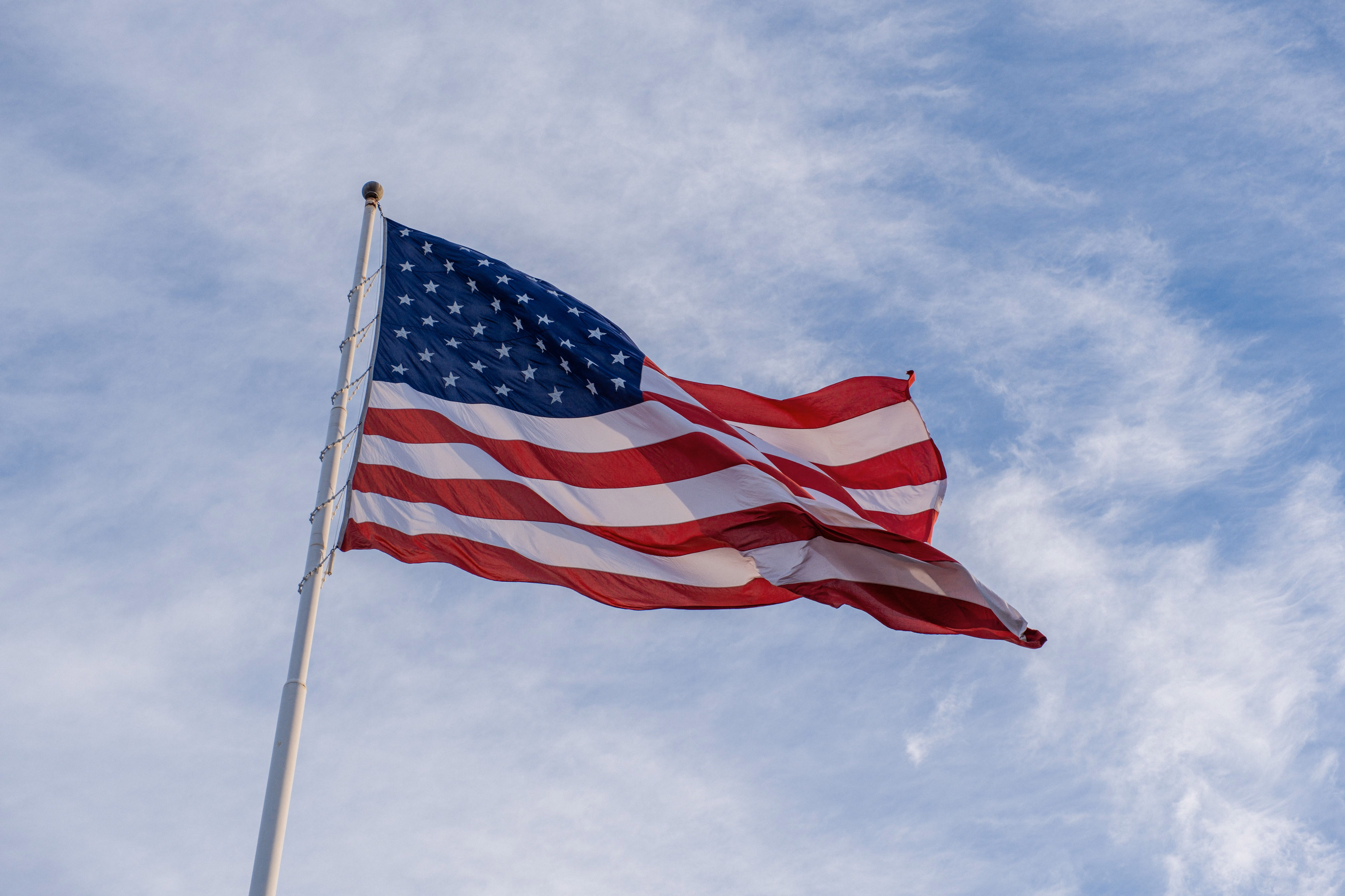 American flag waving on a pole against a partly cloudy blue sky.