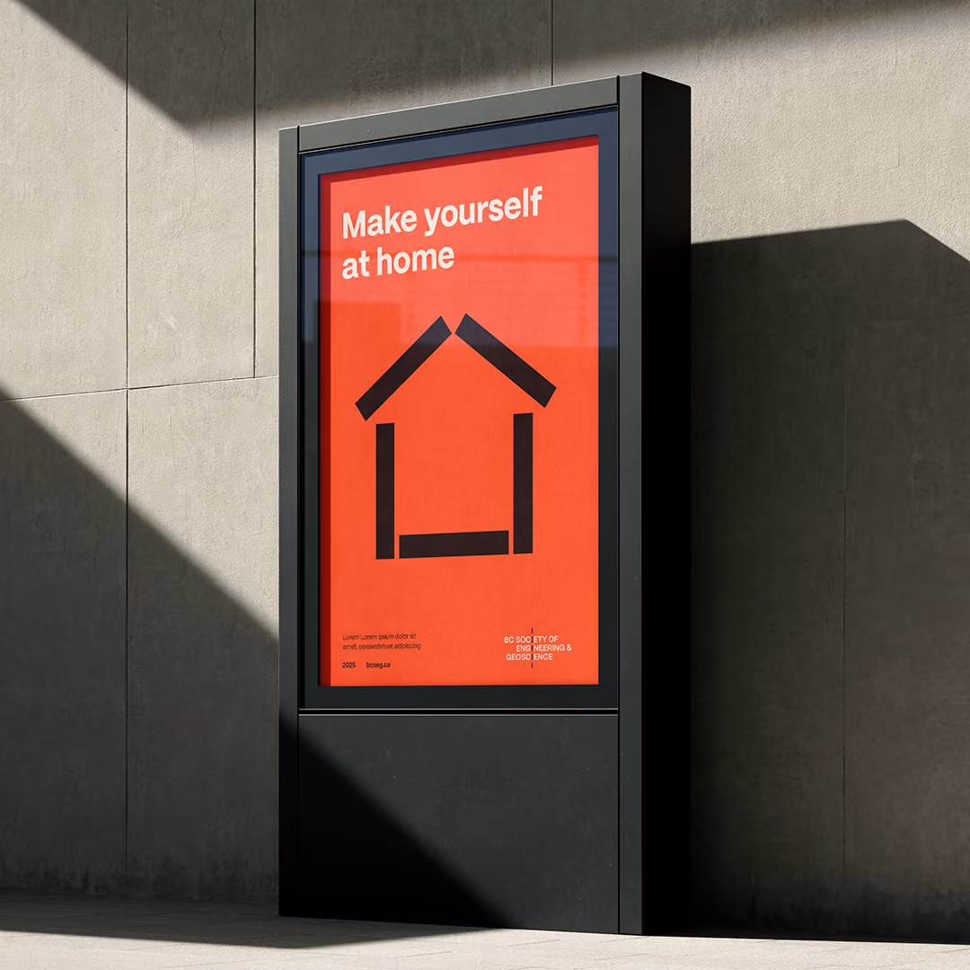 Outdoor digital sign with an orange poster displaying the text 'Make yourself at home' above a simple black house icon made of thick lines, set against a concrete wall with sunlight and shadows.