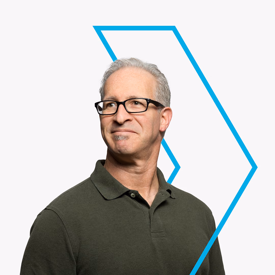 Middle-aged man with gray hair and black glasses wearing a green polo shirt looking slightly right with a faint smile, with a blue chevron outline behind him on a white background.