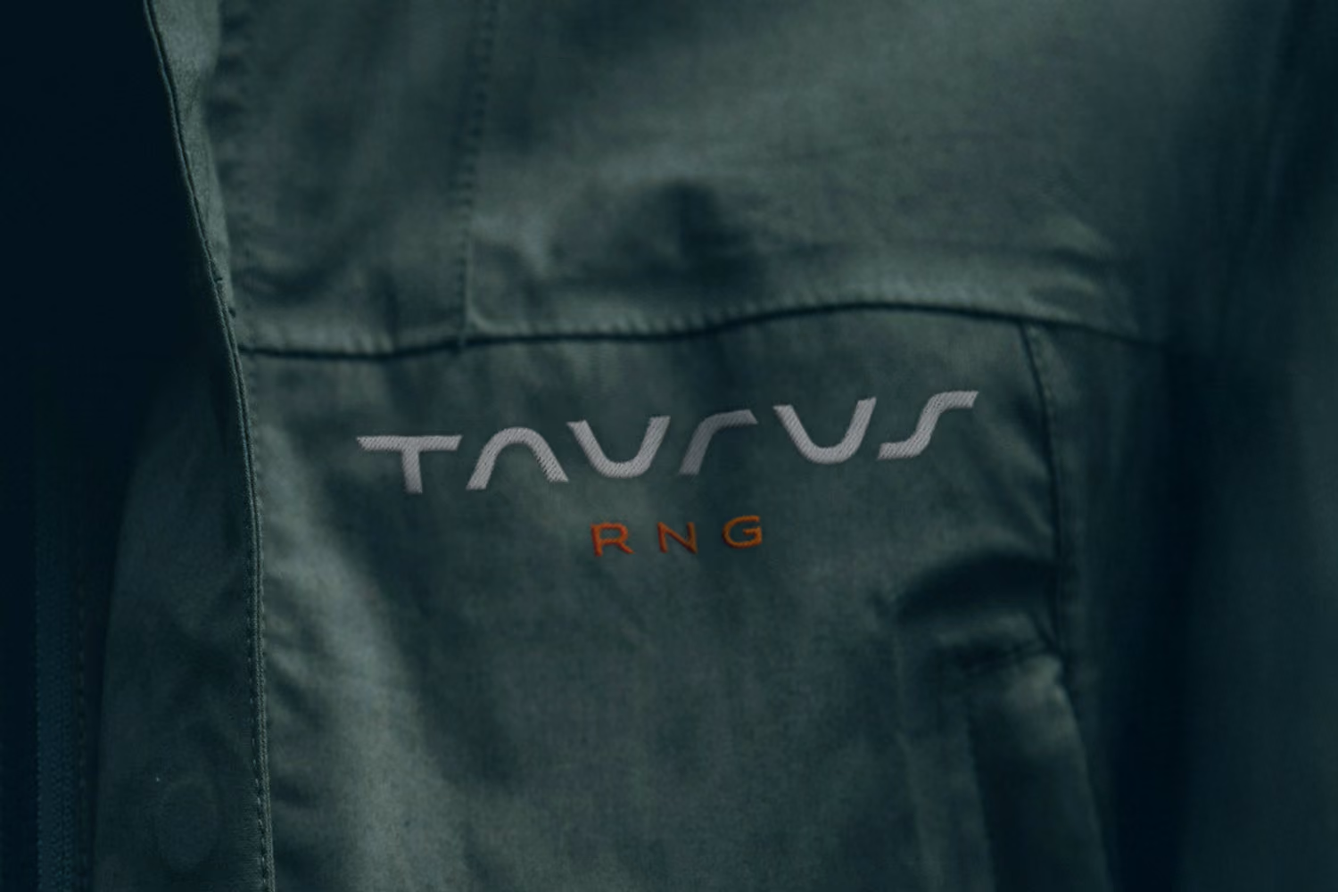 Close-up of fabric with embroidered logo reading 'TAURUS' in gray and 'RNG' in orange.