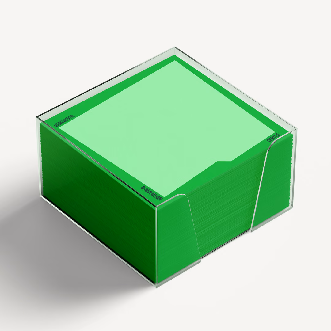 Stack of green sticky notes in a transparent acrylic holder casting a shadow on a white surface. Around the edge of the graphic shape on the cards are the words 'Vancouver', 'Convention ', and 'Centre' in bold uppercase letters.
