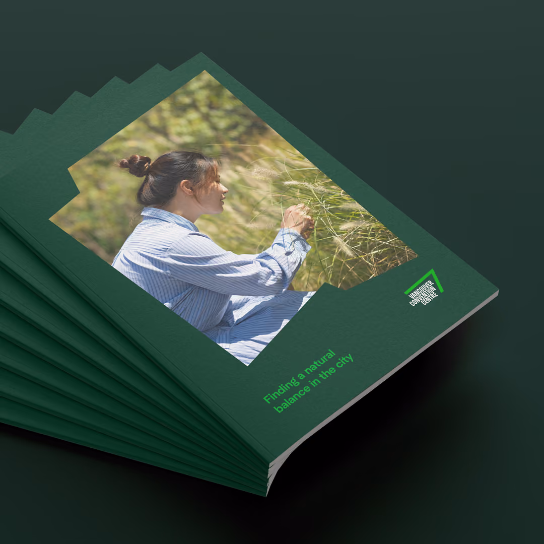 Stack of green booklets with a photo of a woman in a blue striped dress sitting outdoors and touching grass, titled 'Finding a natural balance in the city' with Vancouver Convention Centre logo on the cover.
