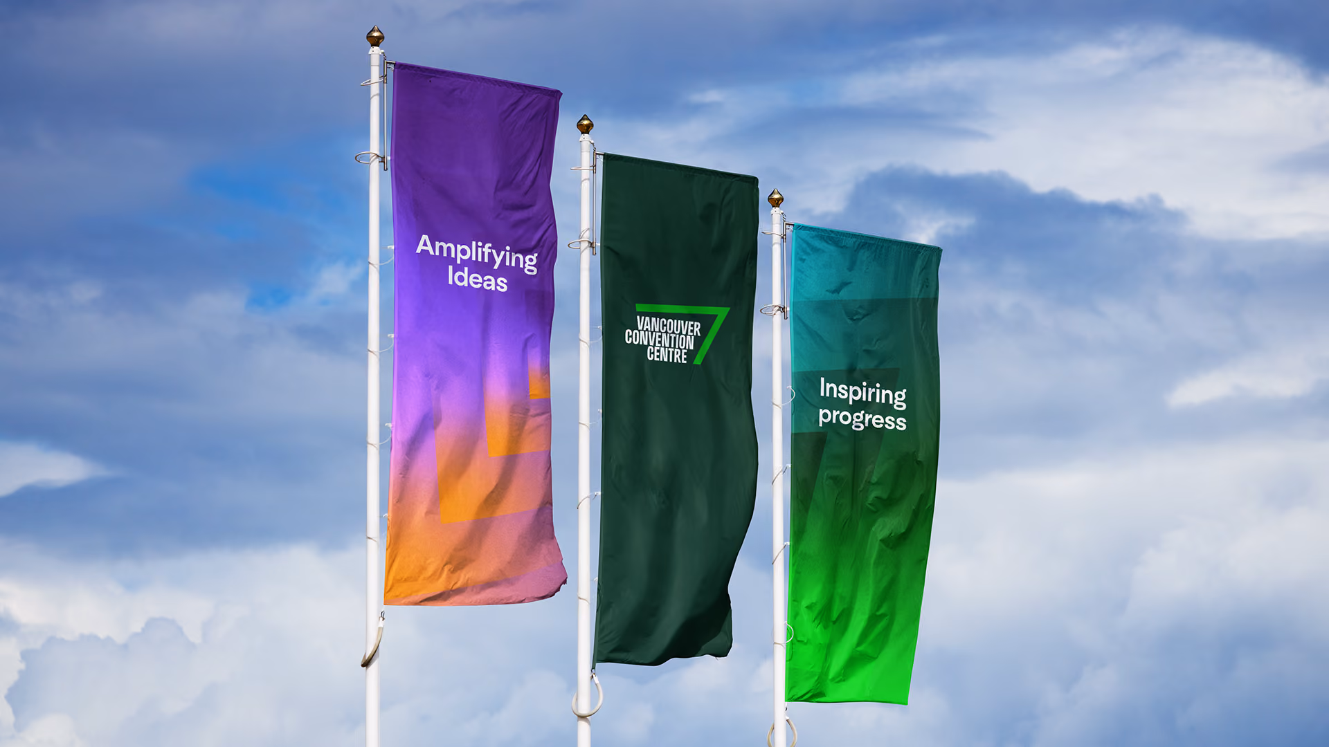 Three vertical flags against a cloudy blue sky: the left flag has a purple to orange radiating gradient with the text 'Amplifying Ideas', the center dark green flag displays the Vancouver Convention Centre logo, and the right flag is green with the text 'Inspiring progress'.