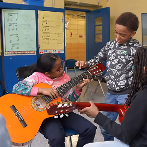 Student and teacher playing guitar together in classroom
