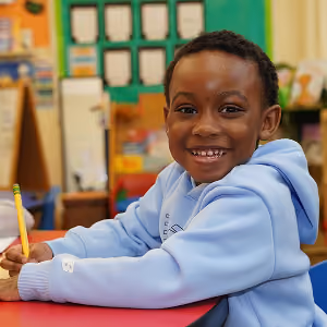 Student smiling while writing at desk in classroom