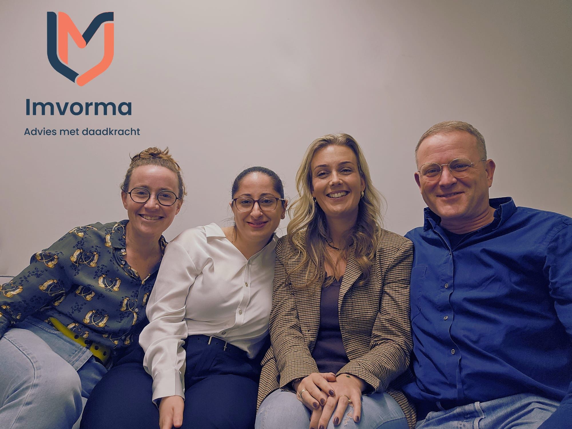 Four people sitting close together and smiling in front of a plain wall with the Imvorma logo and the text 'Advies met daadkracht' above them.