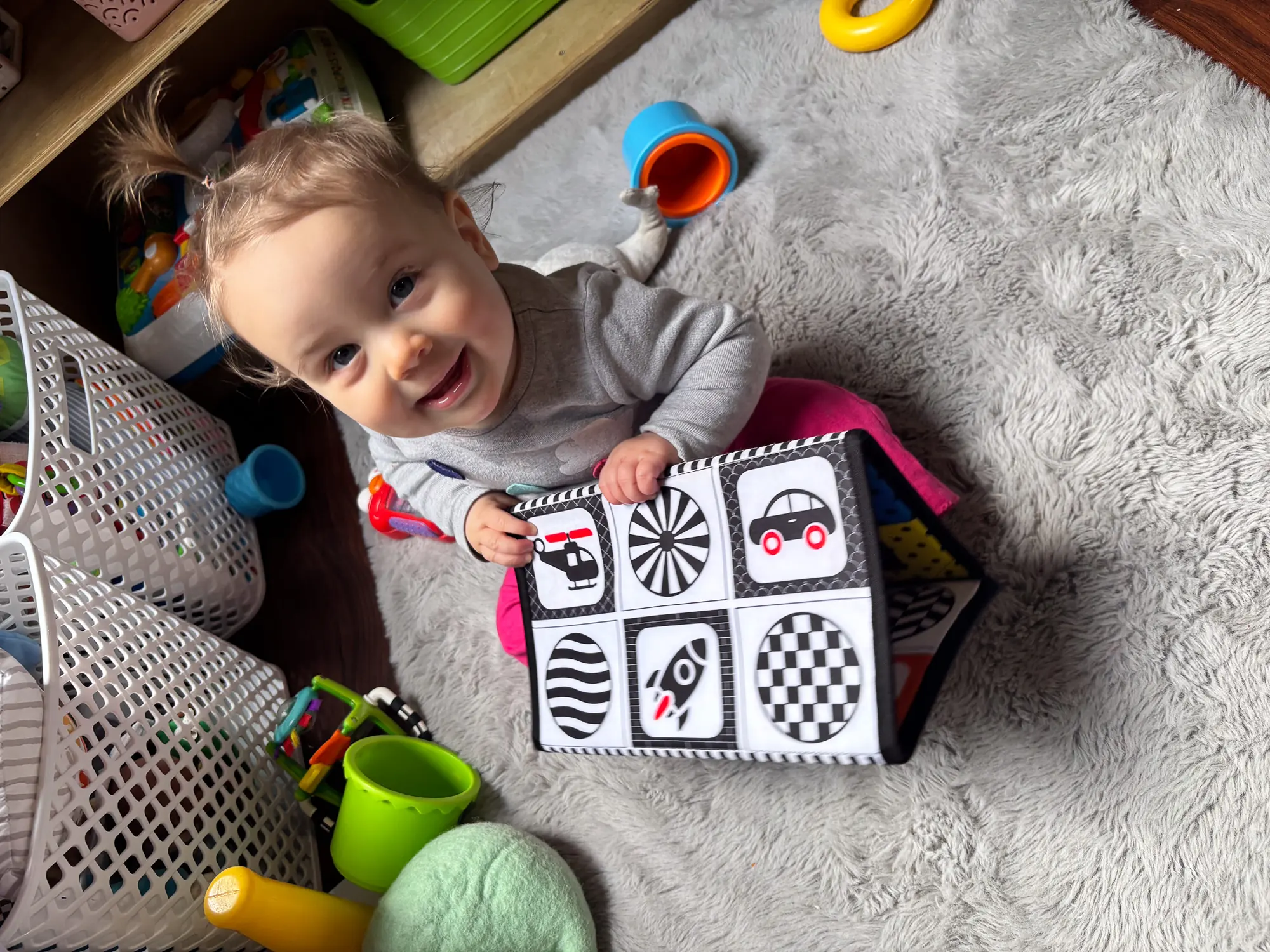 A smiling toddler on a soft rug holding up a black-and-white sensory book
