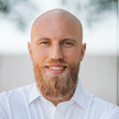 Portrait of a smiling bald man with a red beard wearing a white shirt in a bright indoor setting.