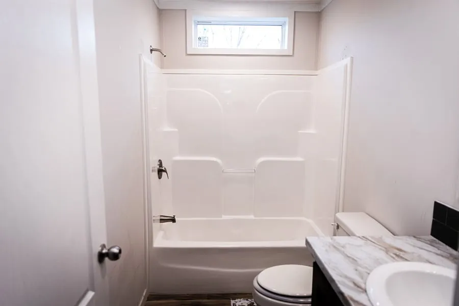 Small bathroom with white bathtub, shower fixtures, window above, toilet, and countertop sink.
