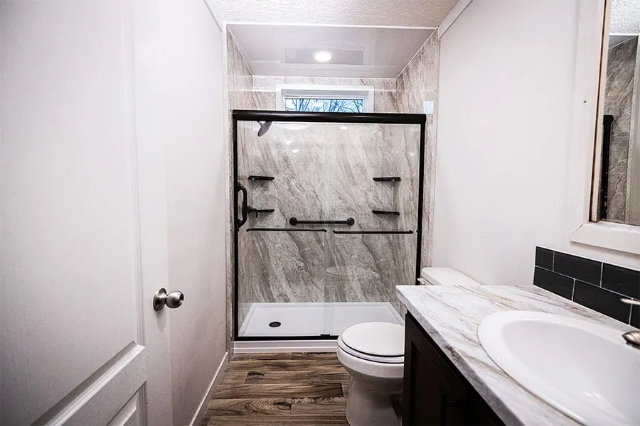 Modern bathroom with glass shower enclosure, marble countertop, white sink, and wooden floor.