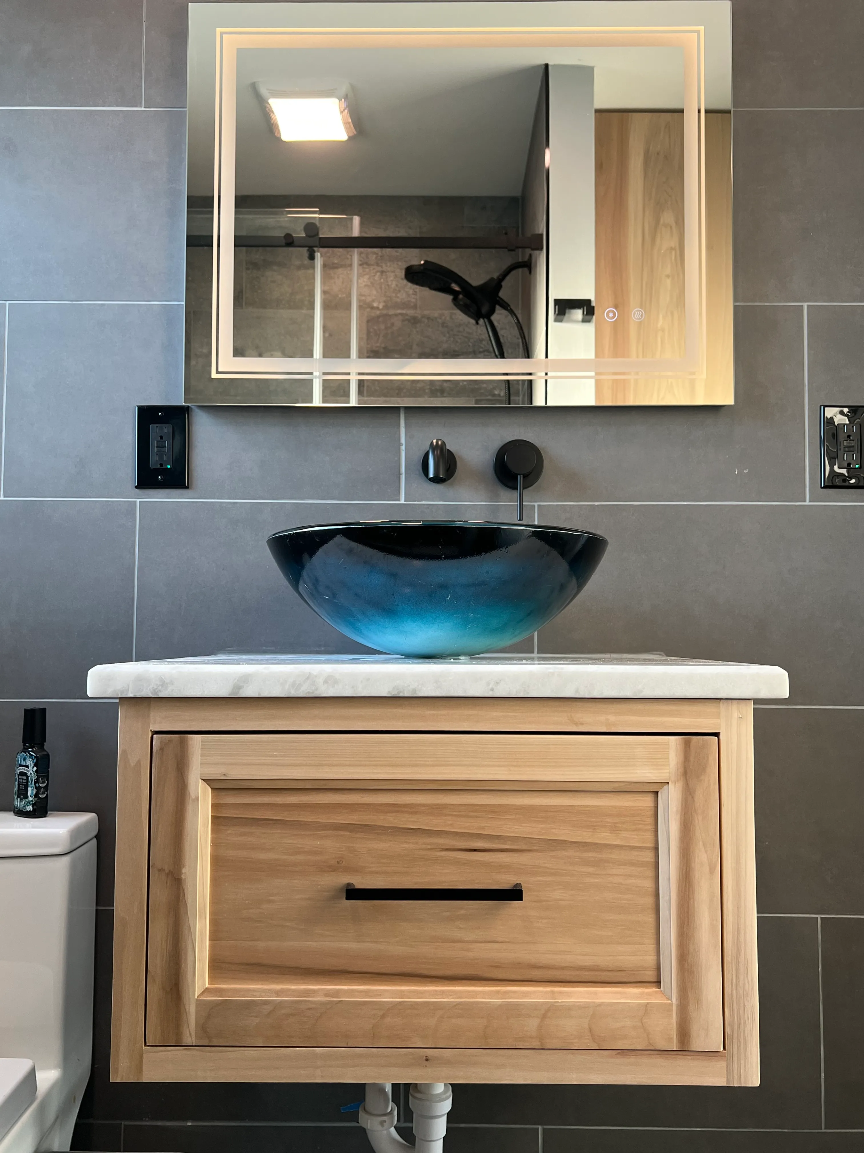Modern white bathroom vanity with black handles, a speckled countertop, and a decorative vase with greenery.
