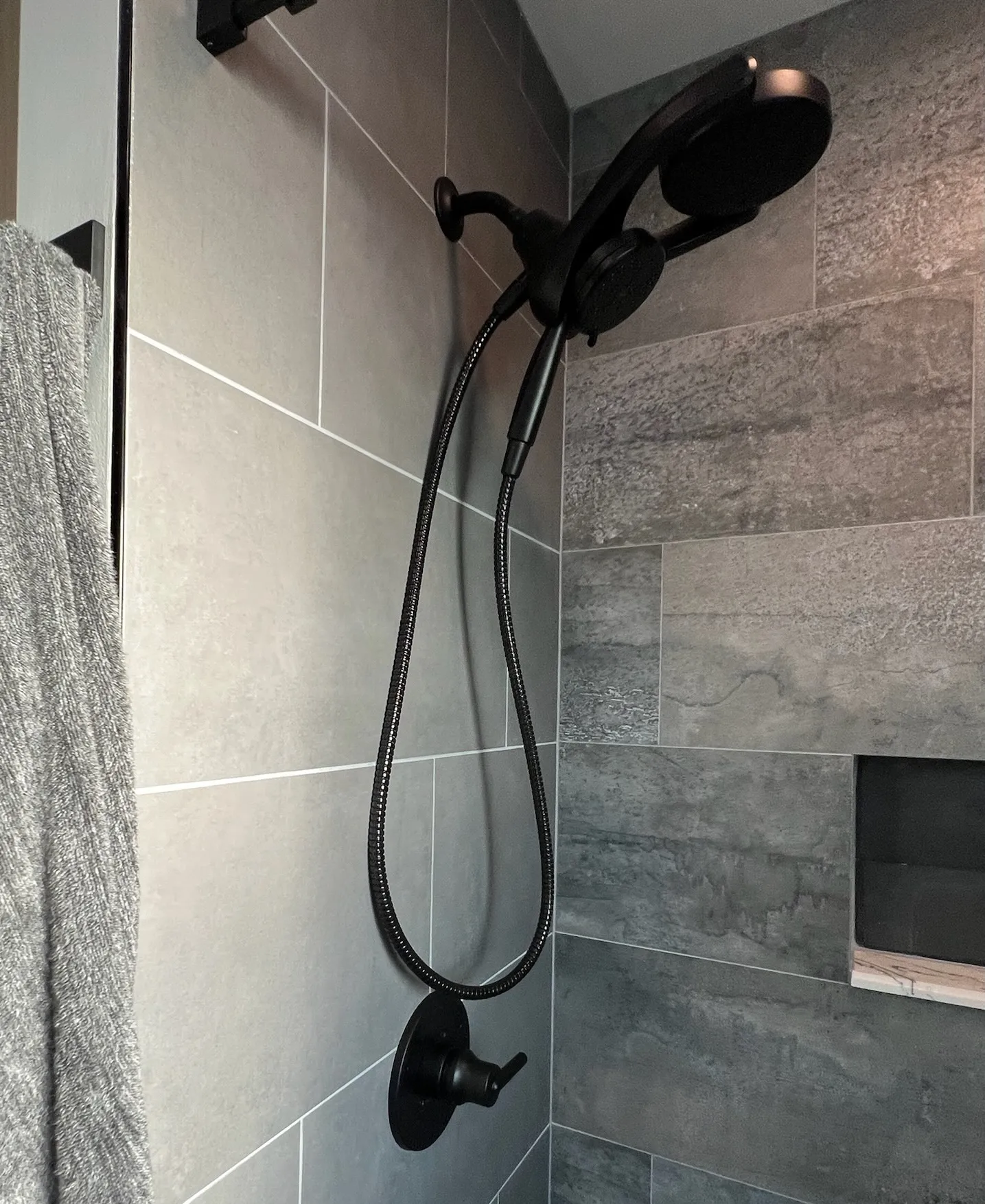 Modern shower with matte black fixtures and rain showerhead on white marble FIBO walls.