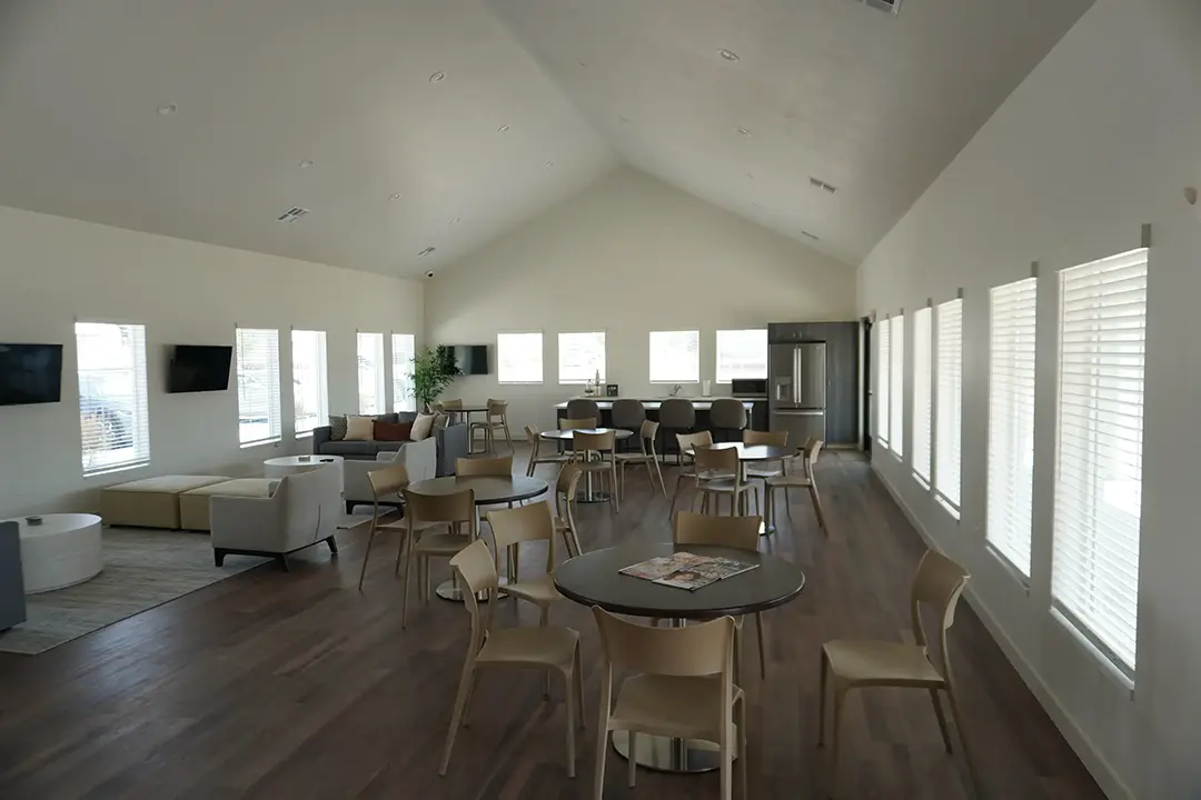 Spacious community clubhouse at Valora Apartments featuring lounge seating, dining tables, large windows, and an open gathering area.