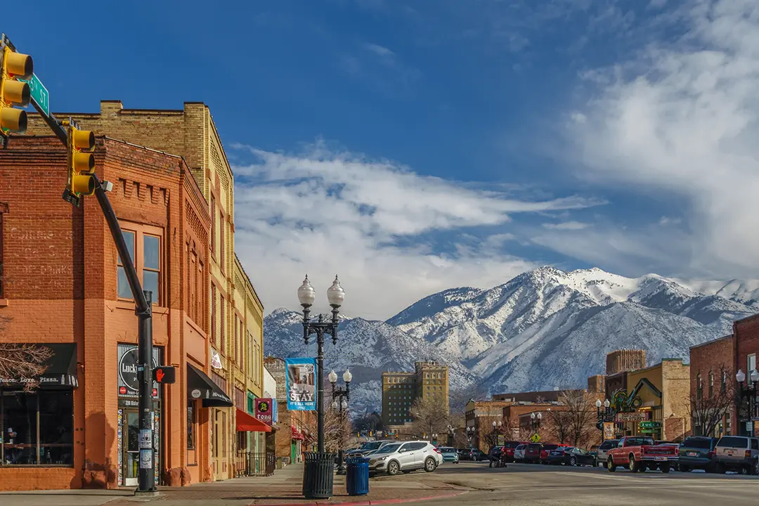 Scenic view of downtown Ogden, Utah, with historic buildings, local shops, and snow-capped mountain peaks in the background.
