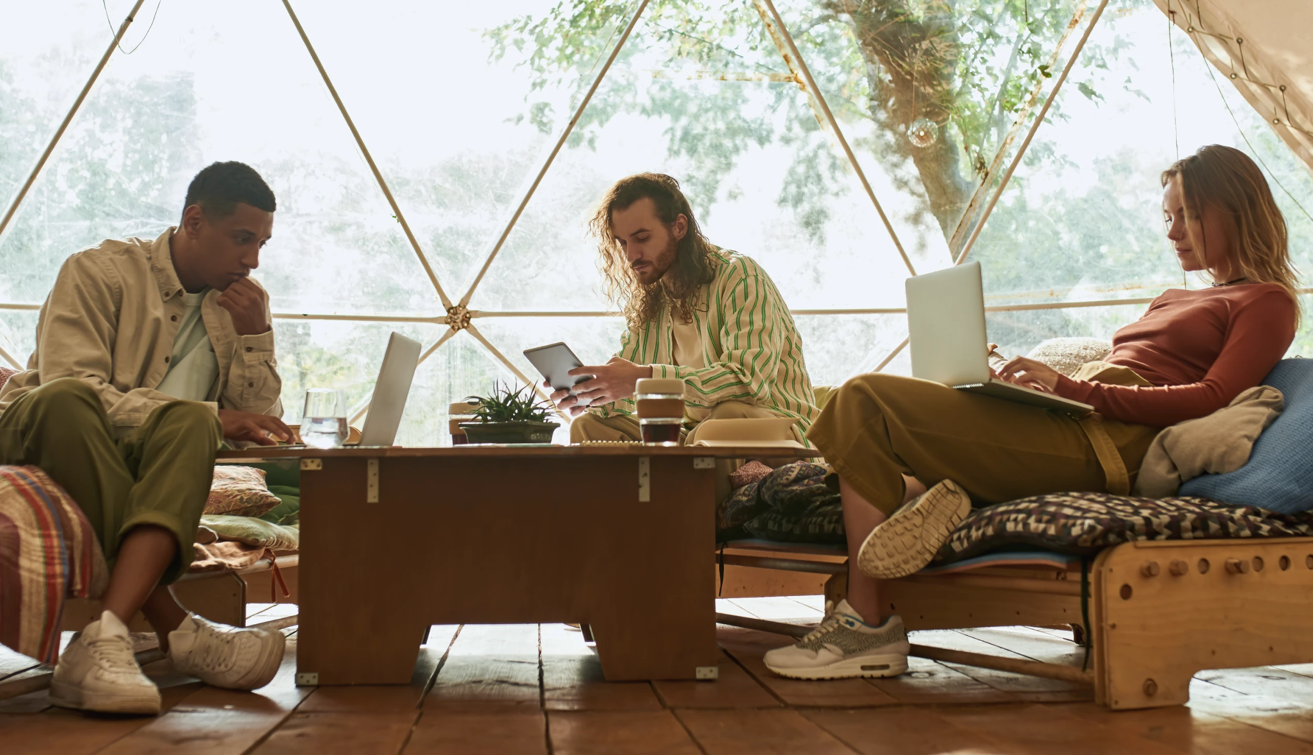 Three people sitting working on devices in a warmly lit room