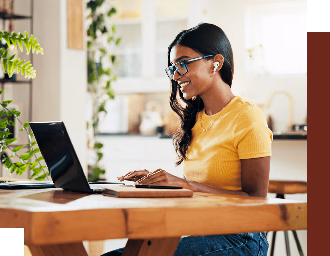 A smiling woman working on a laptop, sitting at a desk in a home.