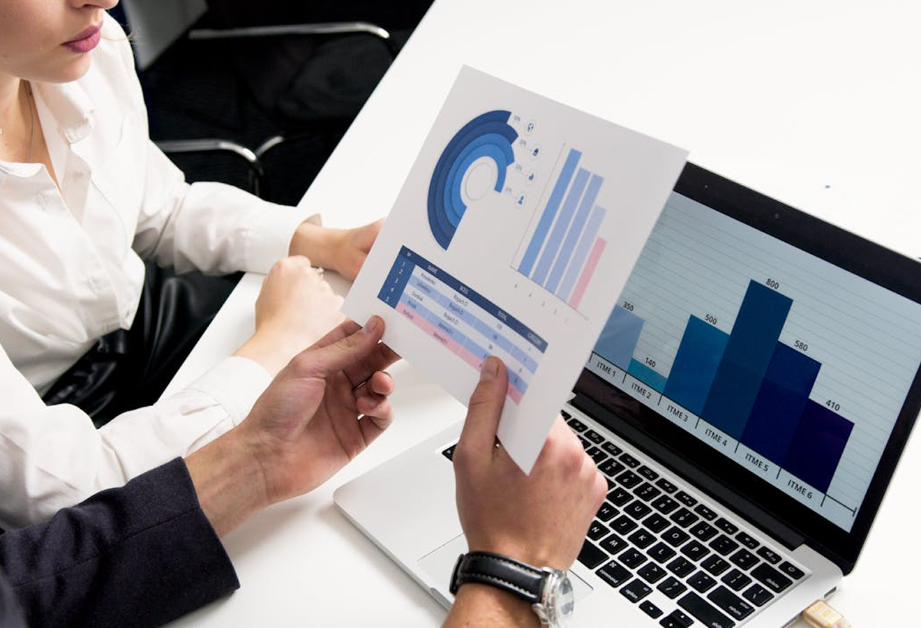 Two people reviewing printed and digital bar and circular charts during a business meeting.