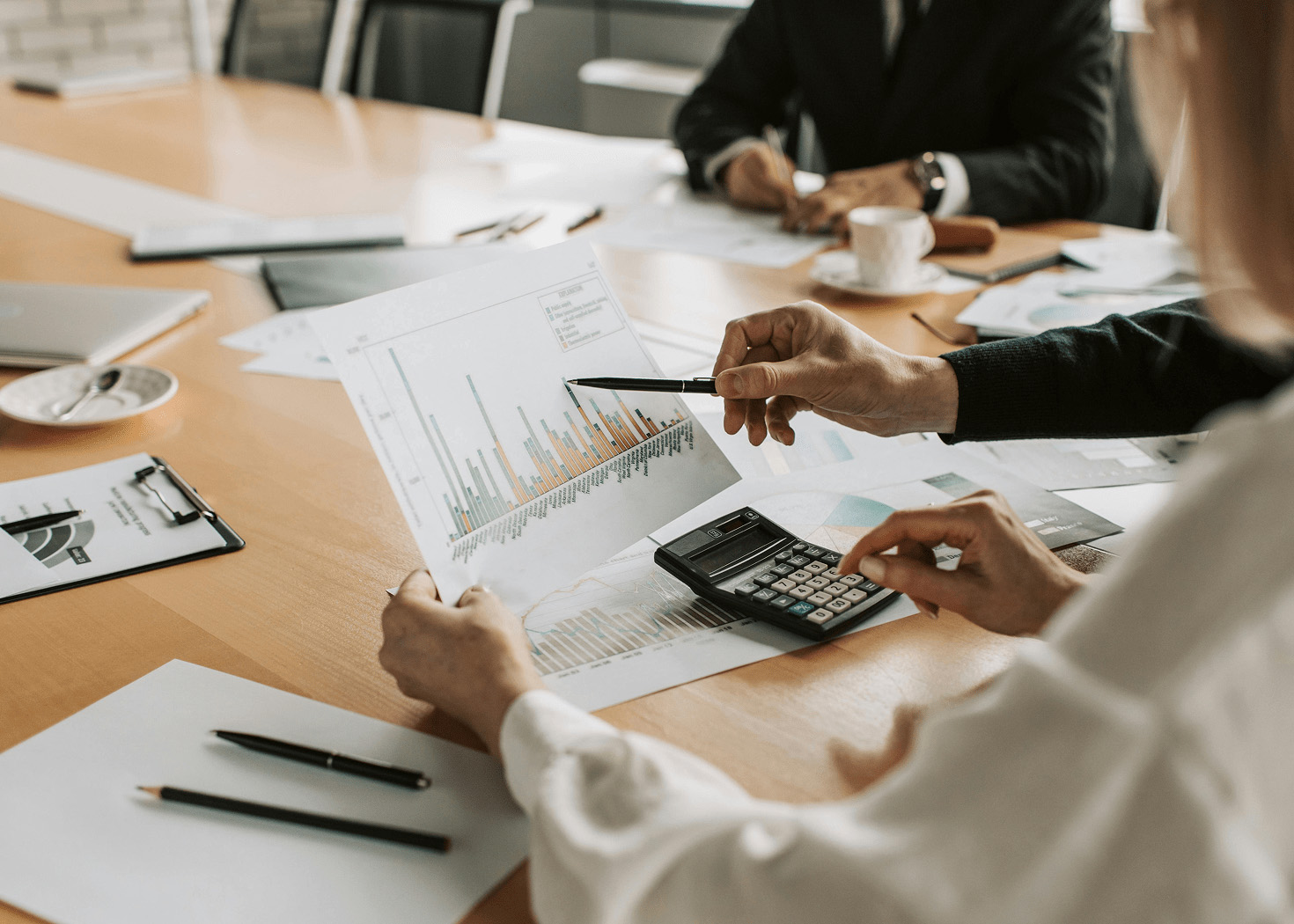 Two people reviewing financial charts and using a calculator at a meeting table.