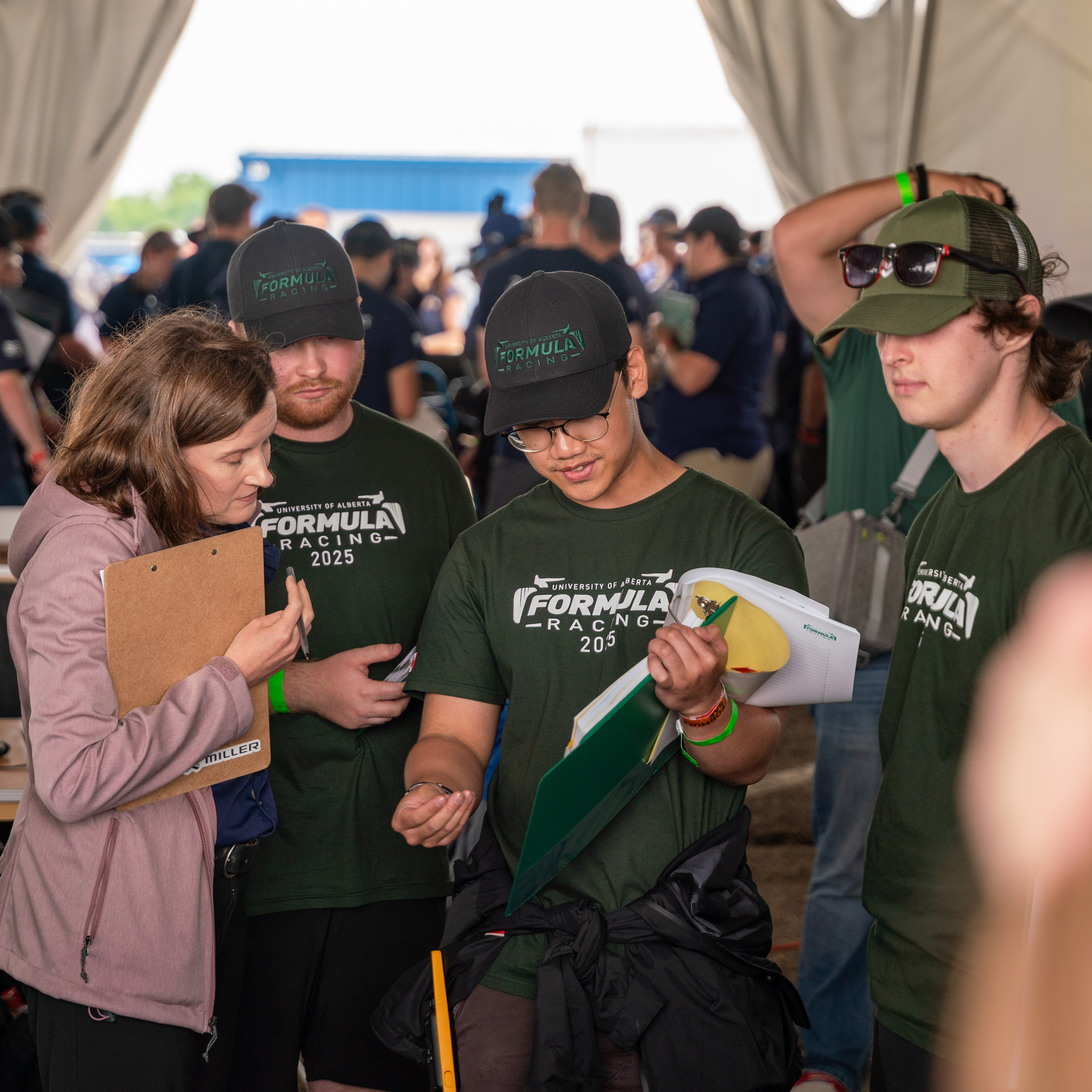 University of Alberta Formula Racing team members discuss with a woman holding a clipboard at an event.