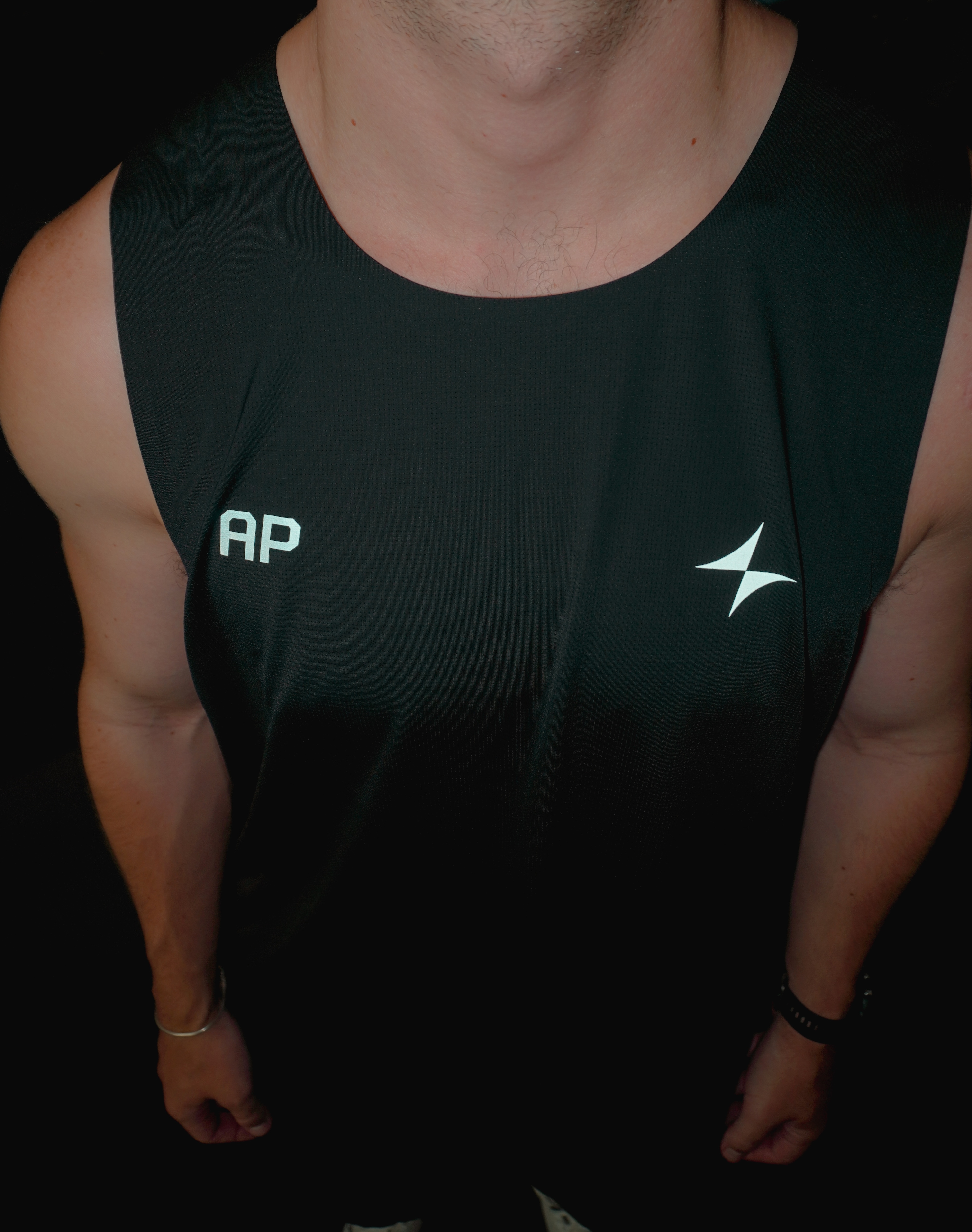 Upper body of a person wearing a black sleeveless athletic tank top with white 'AP' letters on the left chest and a white Arc logo on the right chest.