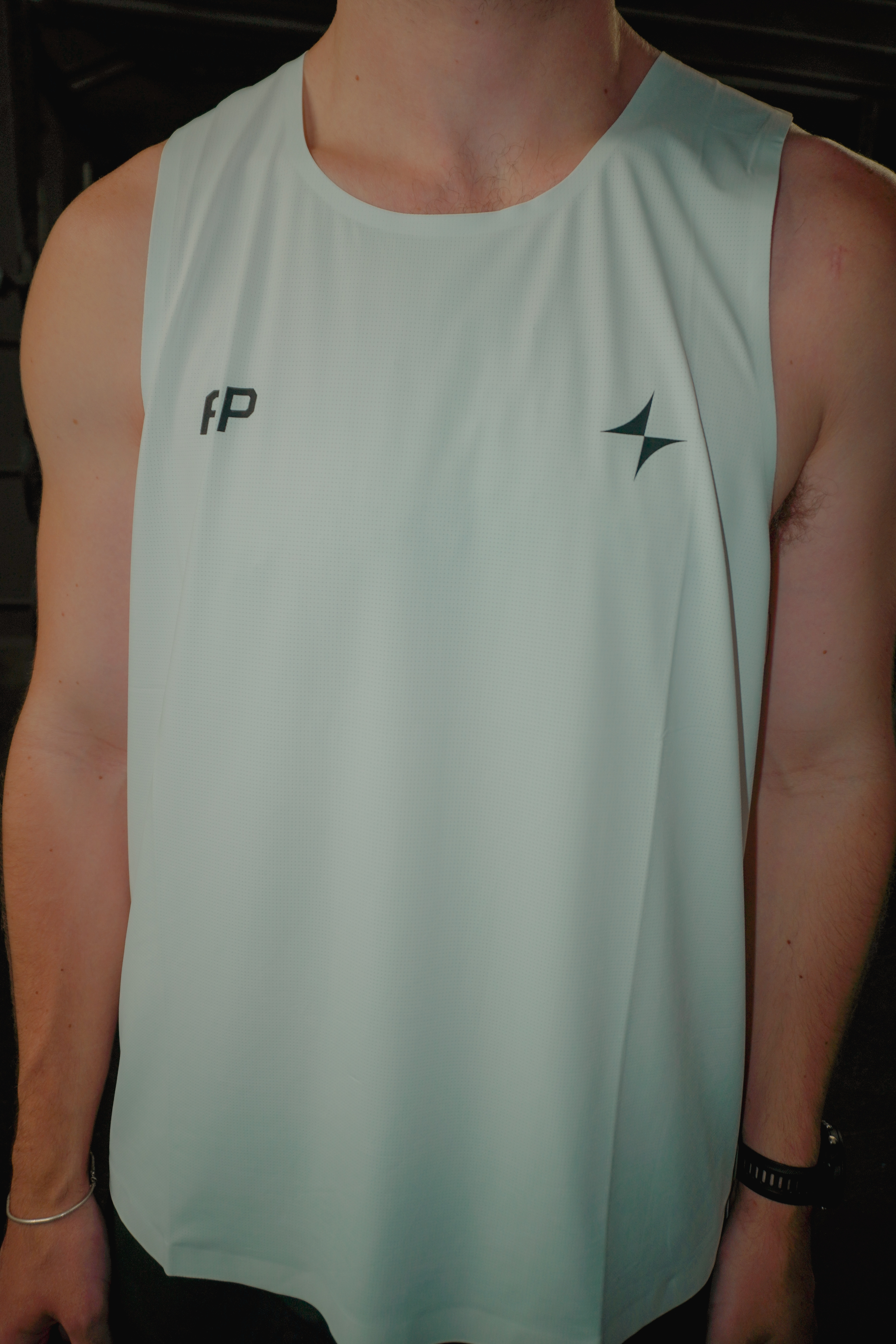 Person wearing a white sleeveless athletic tank top with a small logo on the left chest and initials 'AP' on the right chest.