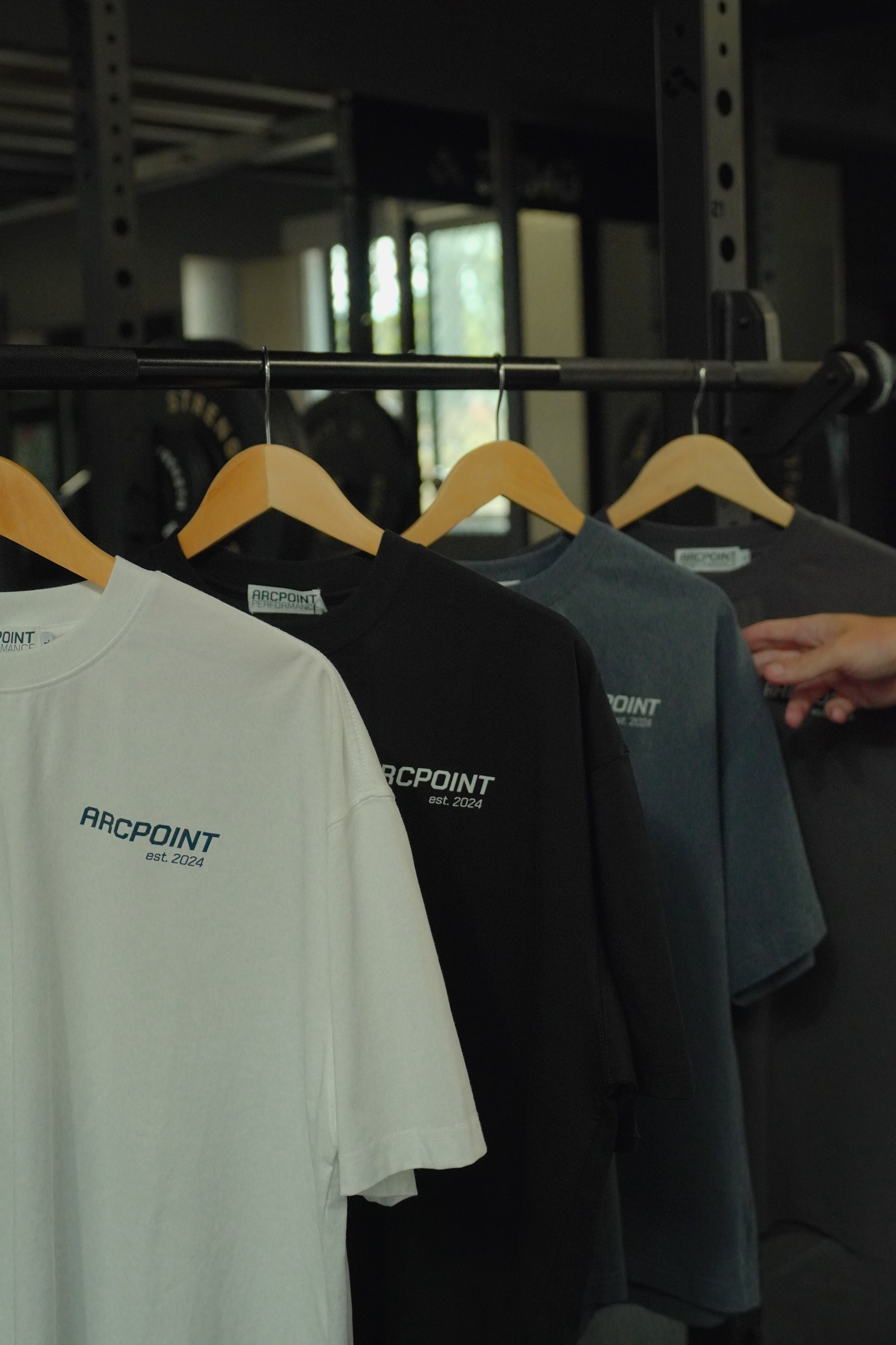 White sleeveless athletic shirt with AP logo and Arc symbol hanging on a black hanger in a gym.