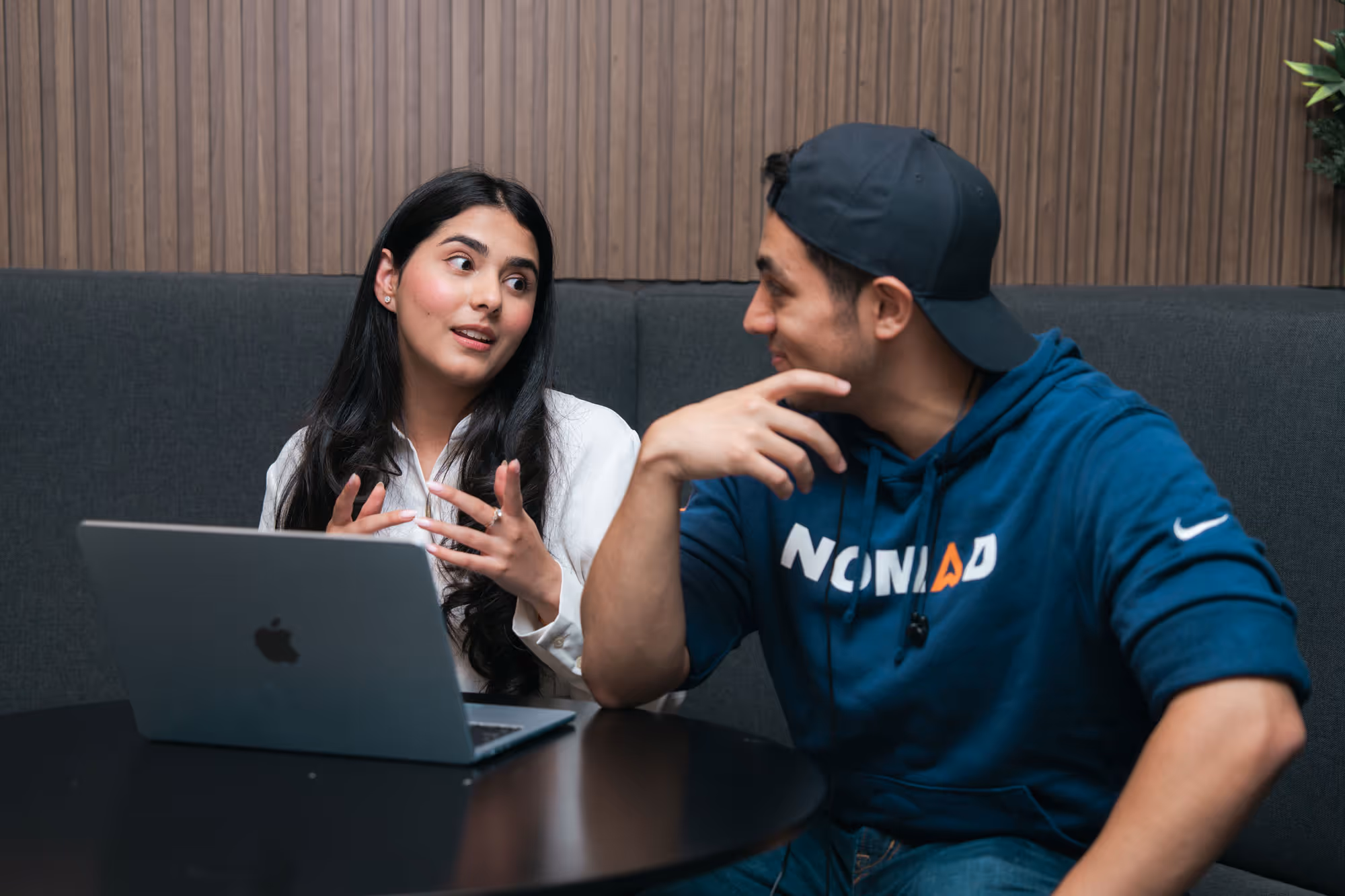 Two people sitting at a table with a laptop, engaged in conversation.
