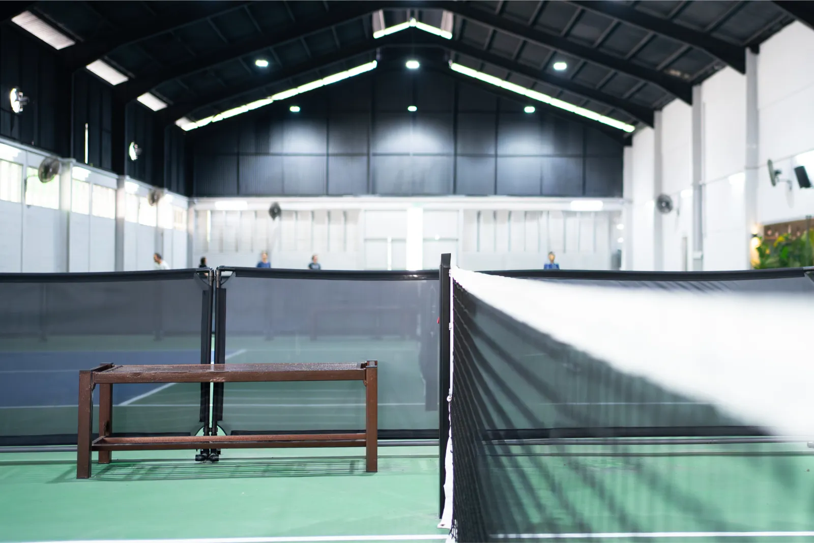 Indoor badminton court with net and empty bench under bright overhead lights.