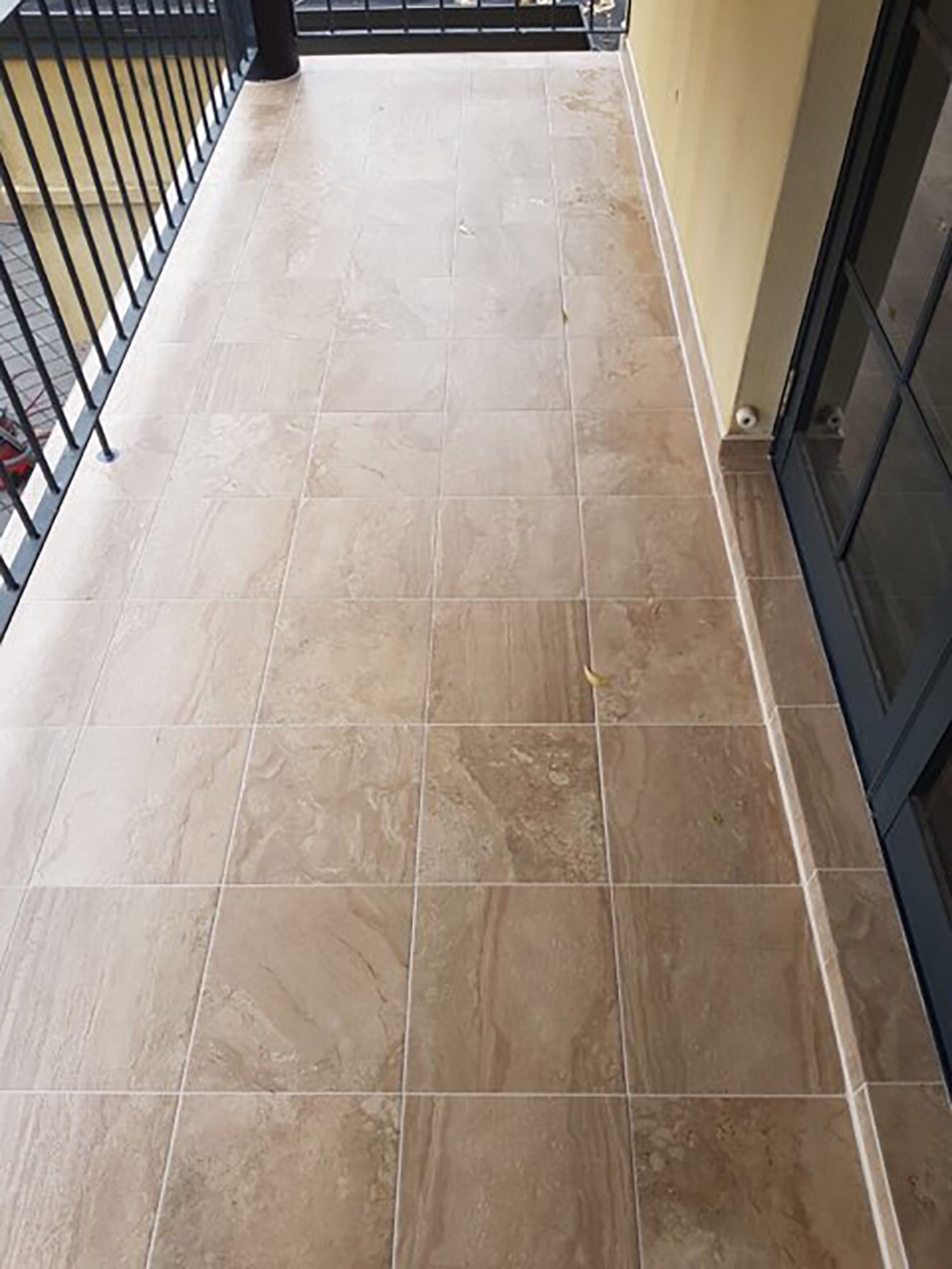 Balcony with beige stone tile flooring, black metal railing on the left, and glass doors on the right.