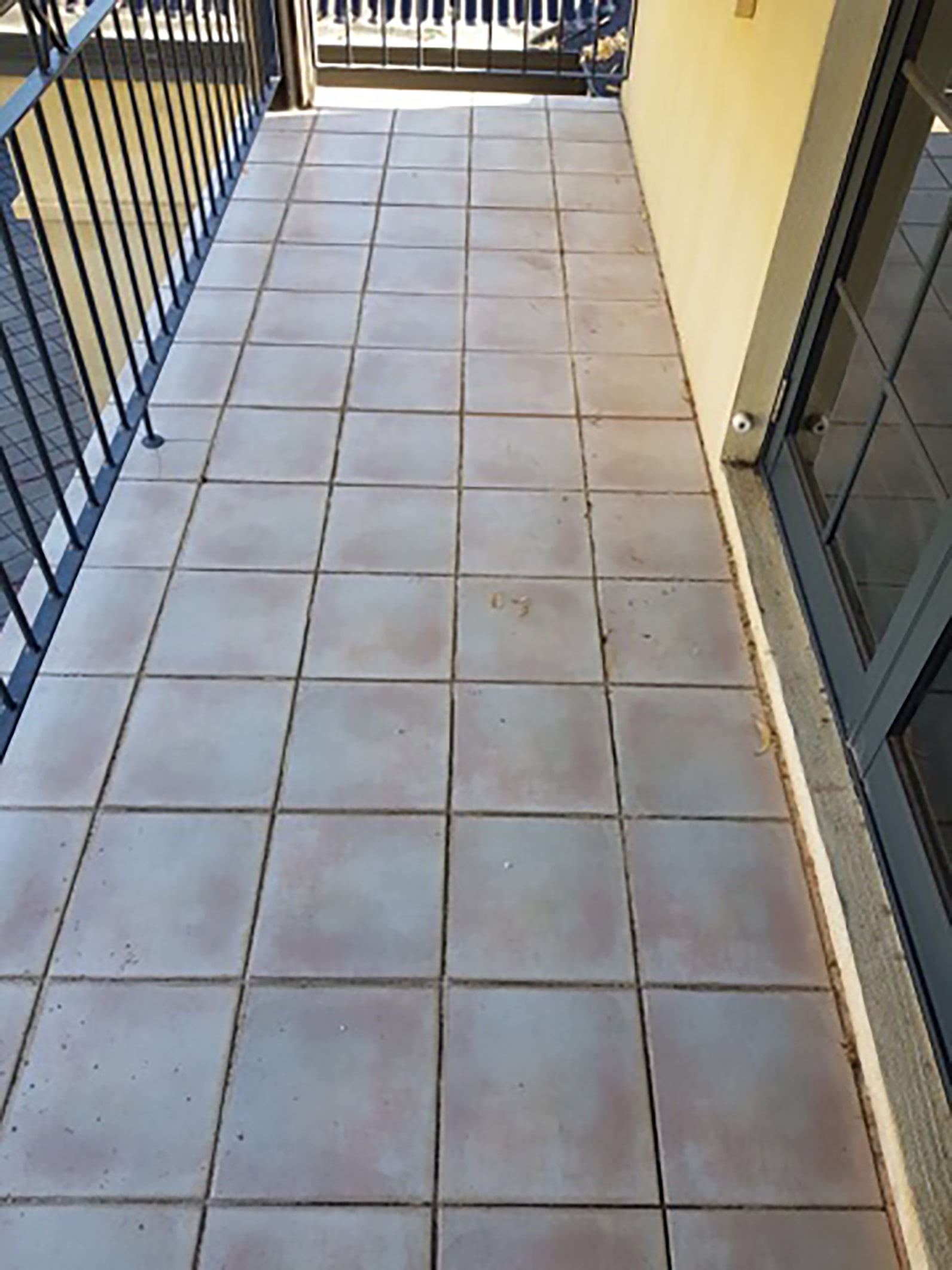 Empty balcony with light gray square tiles, black metal railing on the left, and a glass door on the right.