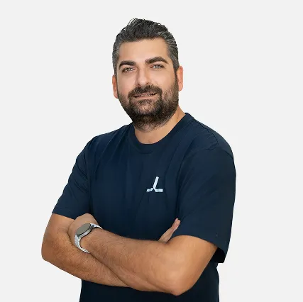Man with short dark hair and beard wearing a navy blue t-shirt with crossed arms, smiling slightly.