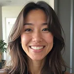 Smiling woman with long dark hair indoors near a window.