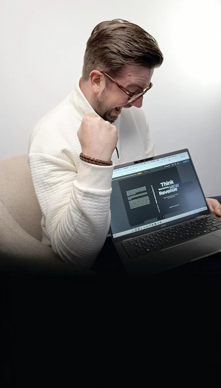 Sascha Albrink feiert den eigenen Erfolg, während er einen Laptop mit seinem digitalen Buch mit dem Titel „Think Marketing New Revenew” in der Hand hält.